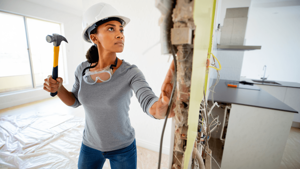 Un homme avec ses équipements de protection en train d'abattre une cloison à l'aide d'un marteau
